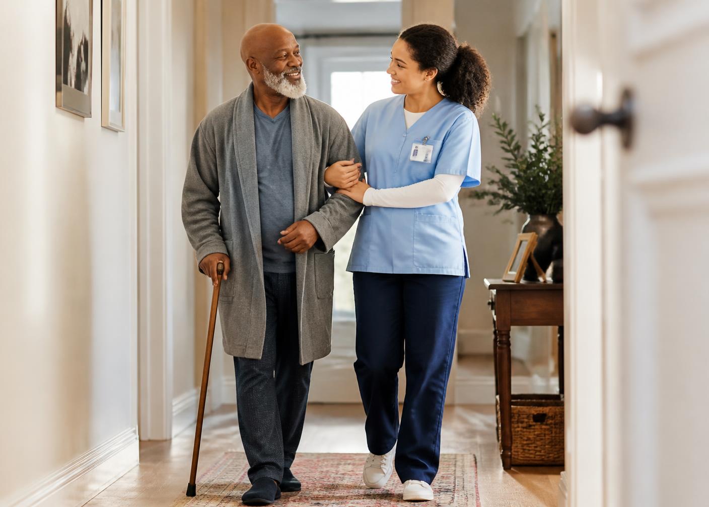 A caregiver steadying an older man as he walks through his home